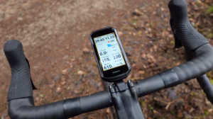 Garmin Edge 1050 am Rennradlenker bei nasser Fahrbahn; auf dem Display sind mehrere Trainingsdatenfelder sichtbar, darunter Timer, Distanz, Puls, Geschwindigkeit, Anstieg, Kalorien, Höhe und Neigung.