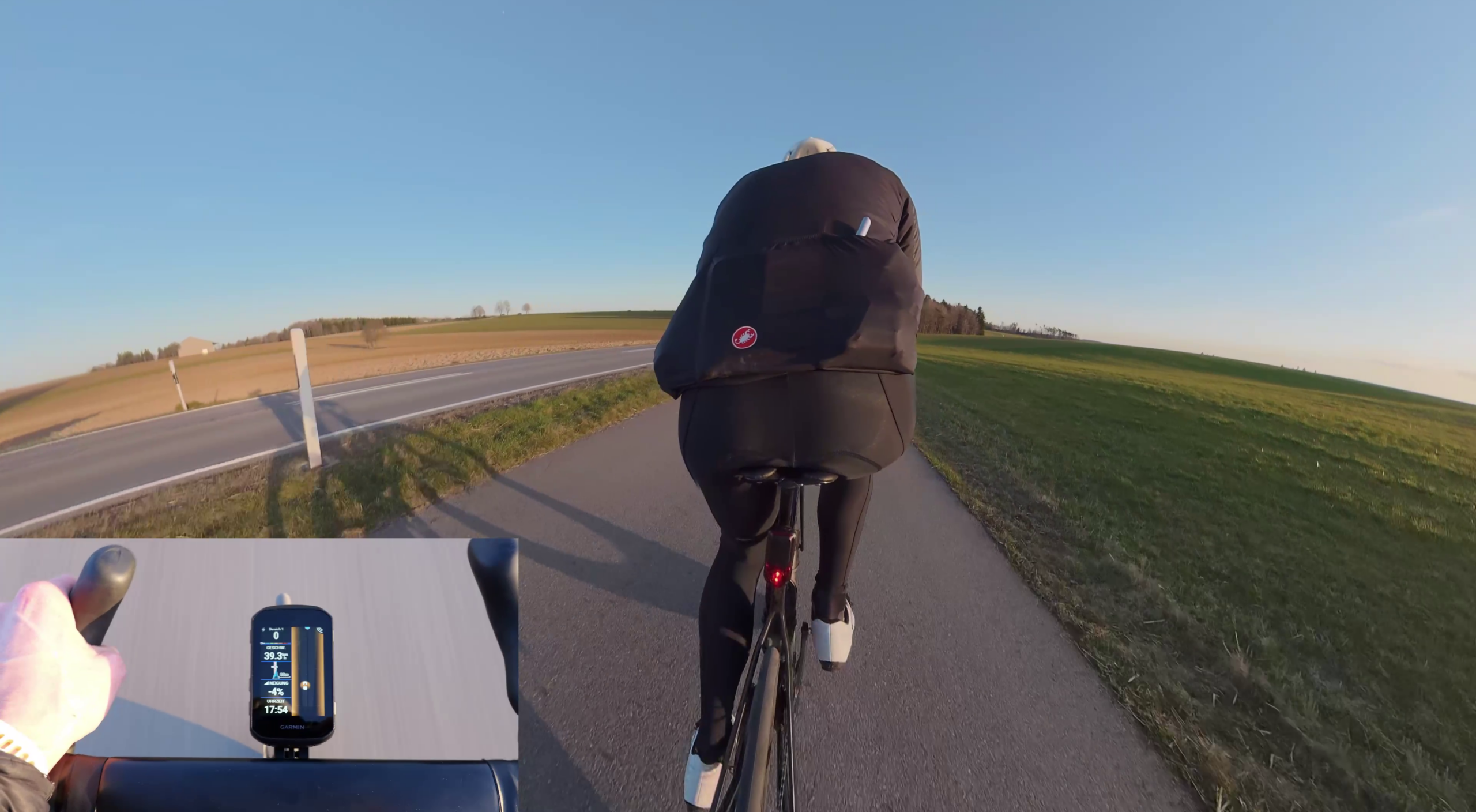 Garmin RearVue820 Test Praxistest des Garmin RearVue 820 im Straßenverkehr: Eine Person fährt auf einem Fahrrad über einen ländlichen Radweg, unten links ist ein eingeblendeter Garmin-Fahrradcomputer mit Radaranzeige zu sehen.