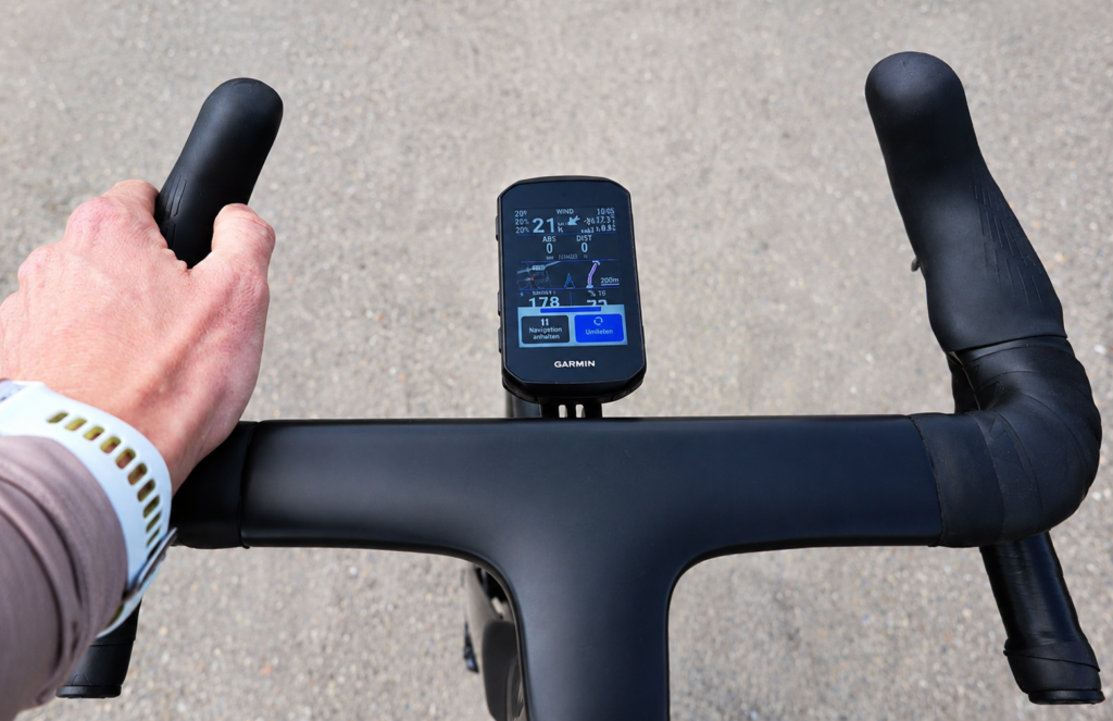 Blick aus der Fahrerperspektive auf einen schwarzen Fahrradlenker mit mittig montiertem Garmin Bike-Computer und einer Hand am Lenker.