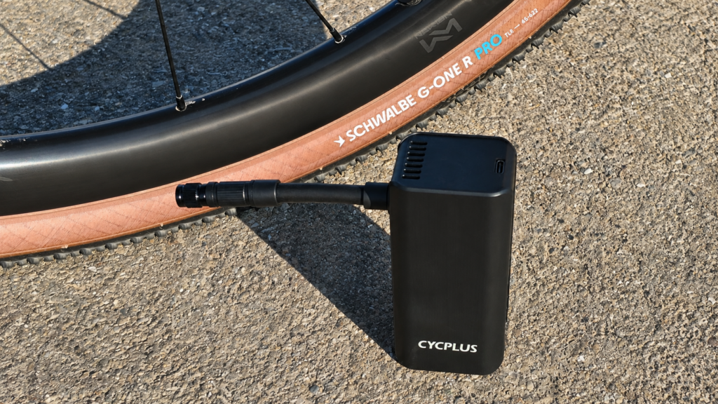 CYCPLUS A3 Mini elektrische Fahrradpumpe mit Luftschlauch neben einem Schwalbe G-One R Pro Gravelreifen.